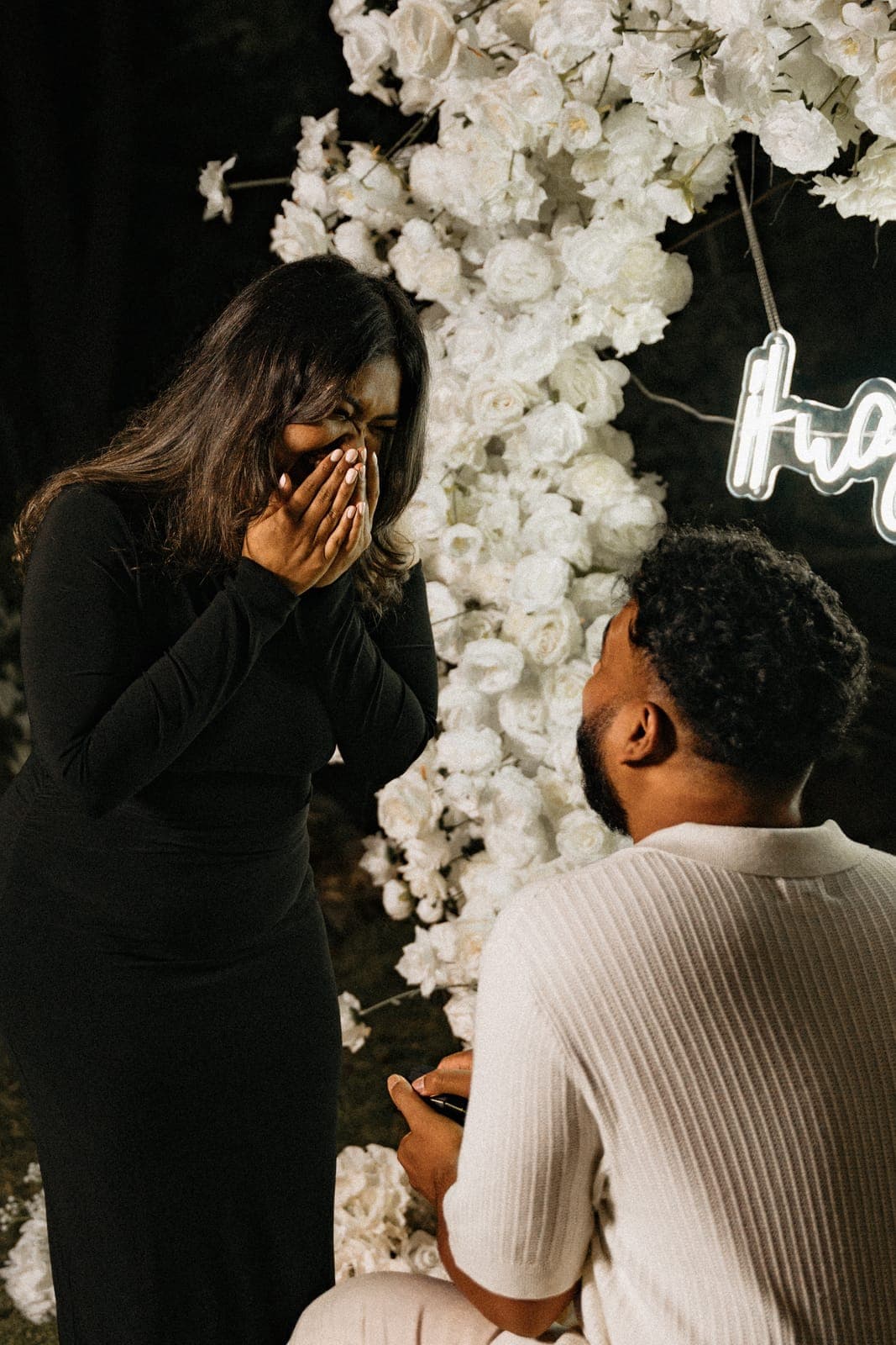 Black-and-white close-up of the proposal moment — Piratheepan kneeling with the ring box as Shivanna covers her mouth in shock and joy