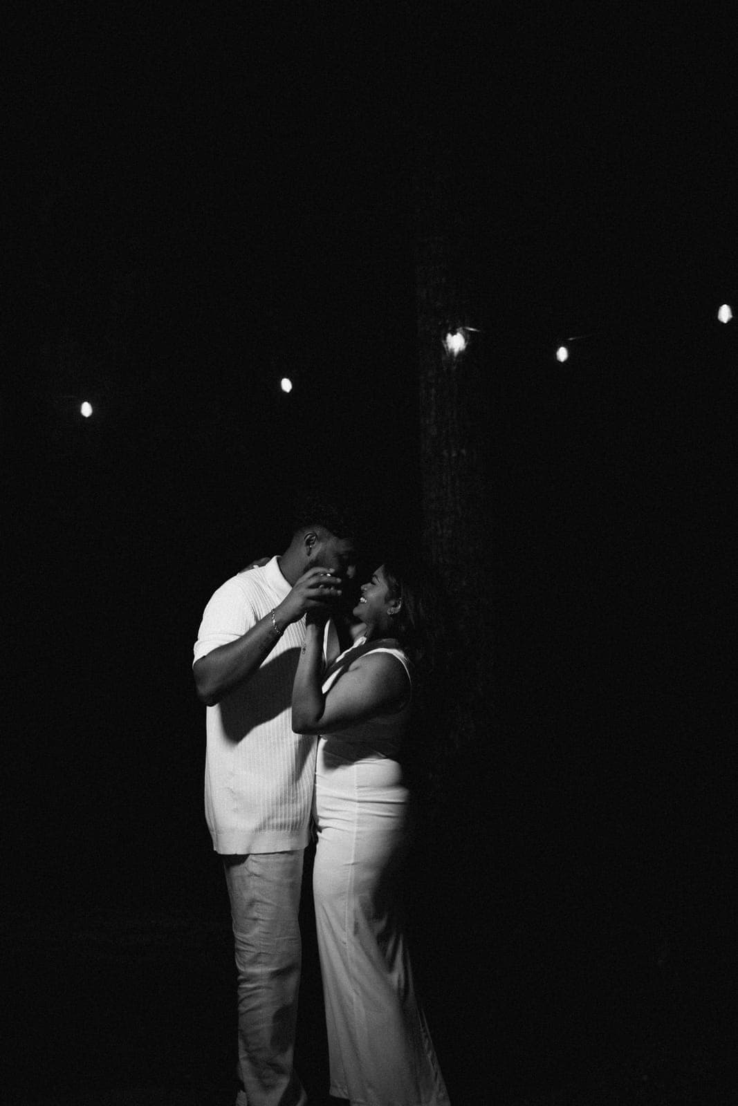 Black-and-white nighttime portrait of Piratheepan and Shivanna embracing under string lights after the proposal